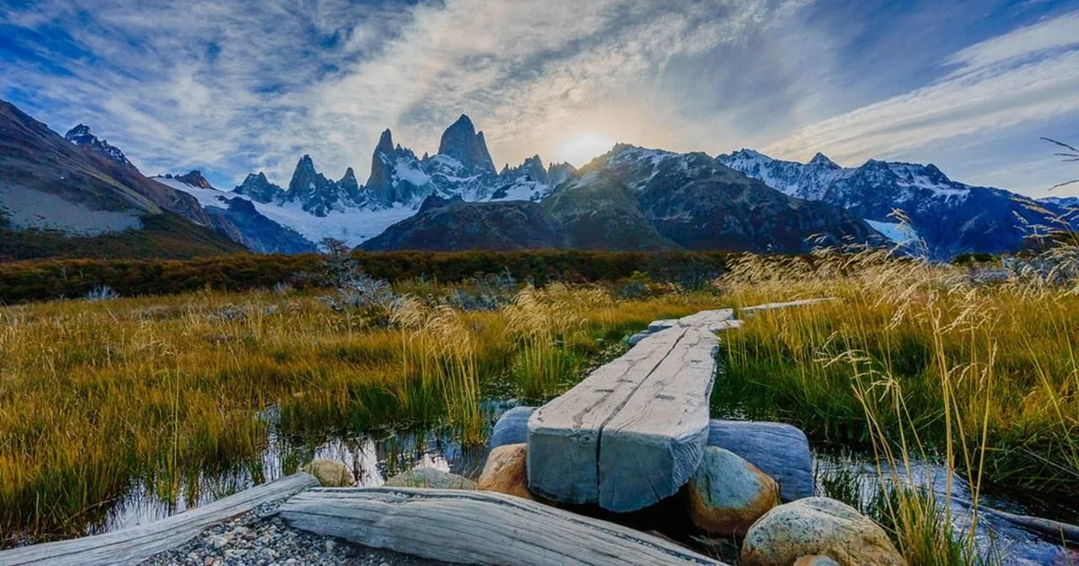 Un caillebotis en bois traversant une prairie dorée vers le massif enneigé du Fitz Roy