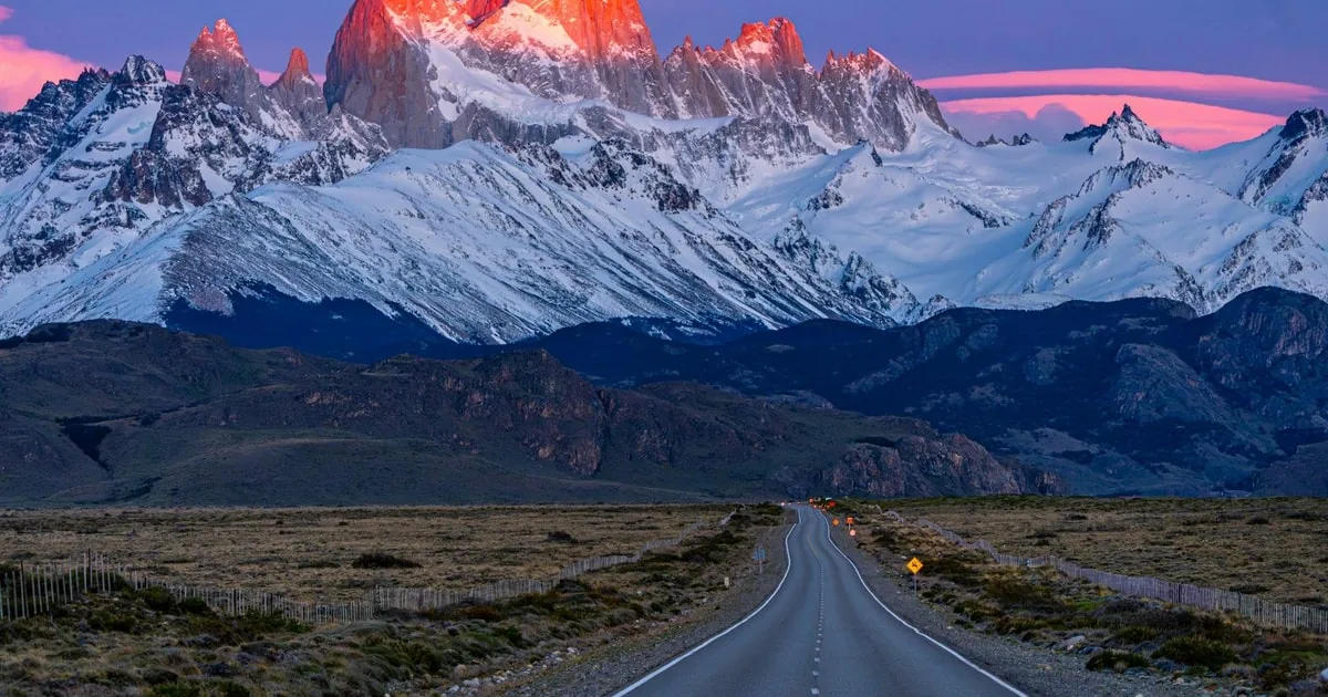 Das Fitz-Roy-Massiv im roten Morgenlicht über einer geraden, leeren Straße
