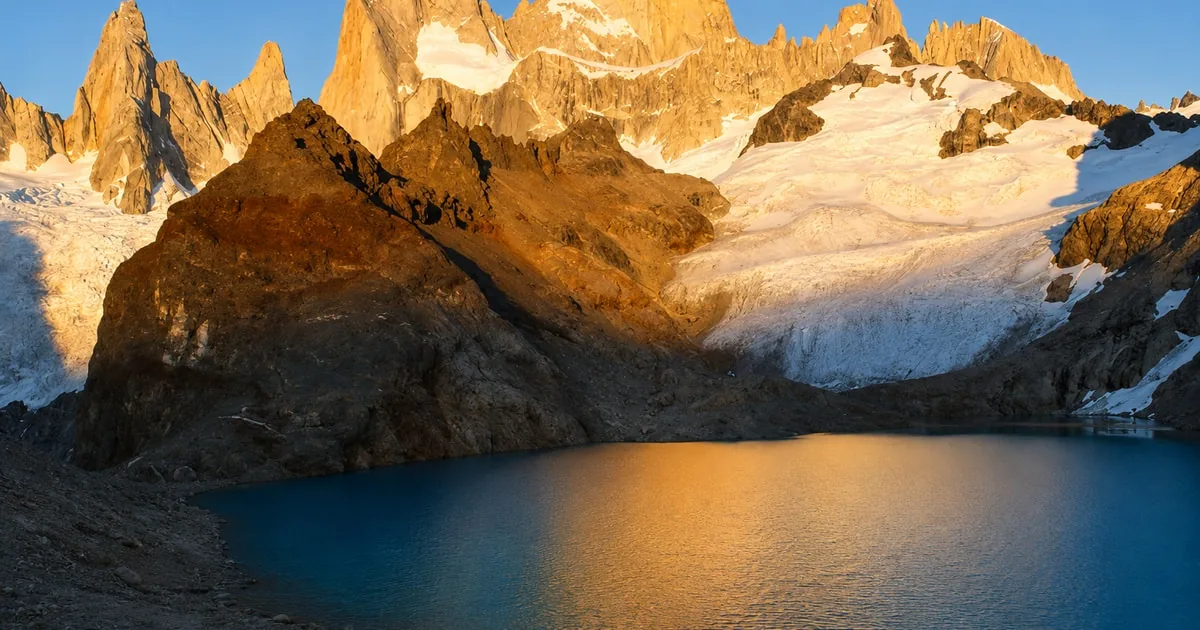Die Granitspitzen des Fitz Roy leuchten orange über einer dunklen Lagune, der Laguna de los Tres
