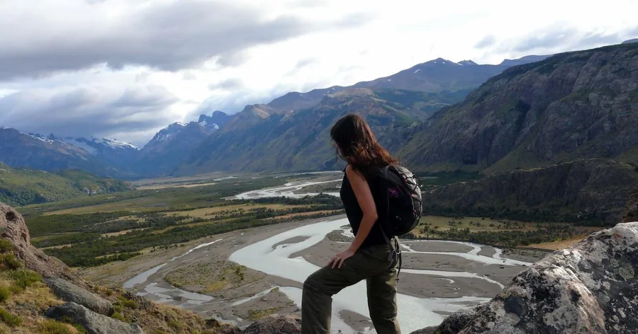 Ein Wanderer auf einem Felsvorsprung mit Blick hinab ins verzweigte Tal des Río de las Vueltas und auf ferne Berge